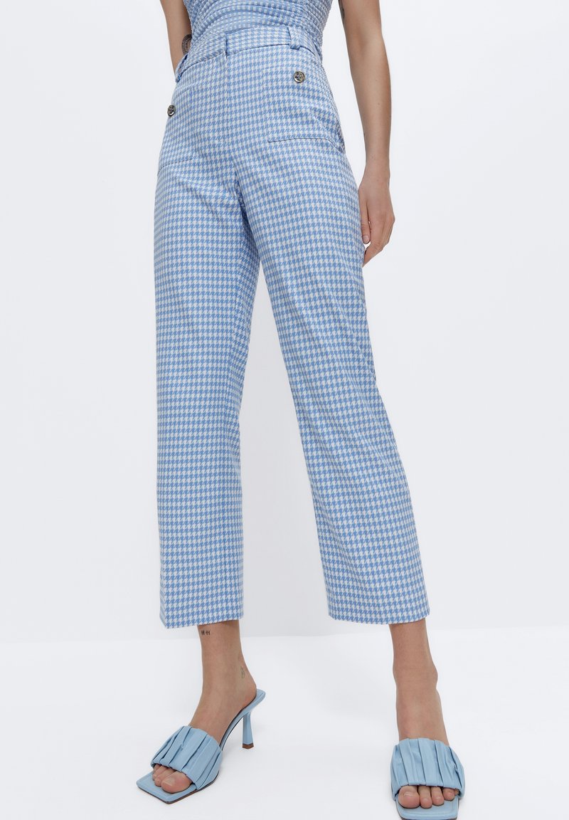 Pantalon à motif pied-de-poule bleu et blanc avec une taille haute, comportant des poches latérales et des boutons en métal brillant. Design cropped et à jambes larges.