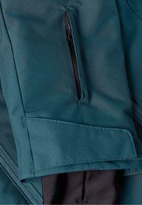 Manche en tissu bleu sarcelle avec une poche zippée noire et un détail de bride Velcro cousu au poignet.
