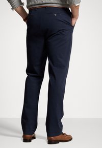 Navy kalhoty z bavlněné směsi, se střihy rovného typu, zadními kapsami a akcentem v podobě knoflíku. Nosené s hnědými botami.