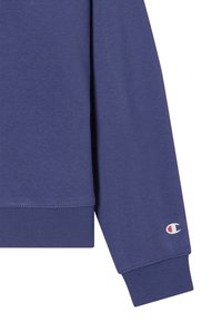 Felpa blu a maniche lunghe con polsini a costine e piccolo logo Champion vicino al polso.