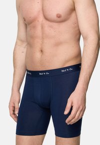 Mörkblå boxerkalsonger gjorda av ett slätt, elastiskt material med en midjeband med logotyp och en figurnära design.