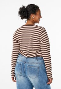 Haut à manches longues rayé en marron et beige, associé à un jean taille haute bleu clair. Texture côtelée avec une coupe décontractée.