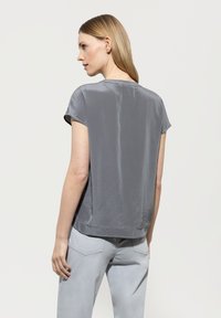 Graues Satinoberteil mit kurzen Ärmeln, leicht lockerer Passform und rundem Ausschnitt, mit glatter Textur und sauberem Saum. Kombiniert mit hellgrauen Hosen.