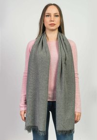 Grå ullsjal med fransade kanter, bärs över en ljusrosa tröja. Sjalen är lång och hänger elegant. Slät textur med en subtil glans.