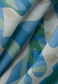 Tessuto di cotone con un motivo a onde in diverse tonalità di blu, verde e beige. La texture appare liscia con una leggera lucentezza.