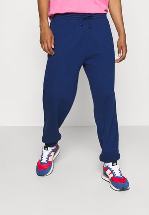 Marineblå sweatpants med elastisk talje og snor, med ribbede manchetter og en afslappet pasform. Kombineret med farverige træningssko.