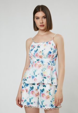 Conjunto de top peplum floral y pantalones cortos en blanco, con flores en tonos pastel, bordes festoneados, tirantes finos y sutiles detalles de escritura.
