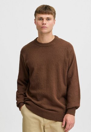 Bruine gebreide trui met een ronde hals, lange mouwen en geribde manchetten. Geweven stof en een ontspannen pasvorm, gecombineerd met lichtbeige broek.