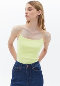 Top in cotone giallo chiaro a costine con spalline sottili, abbinato a una gonna di jeans blu a vita alta. Design semplice e silhouette aderente.