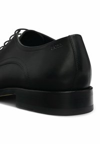 Scarpa da uomo in pelle nera con finitura liscia, cuciture sottili e tacco rialzato e testurizzato con marchio in rilievo.