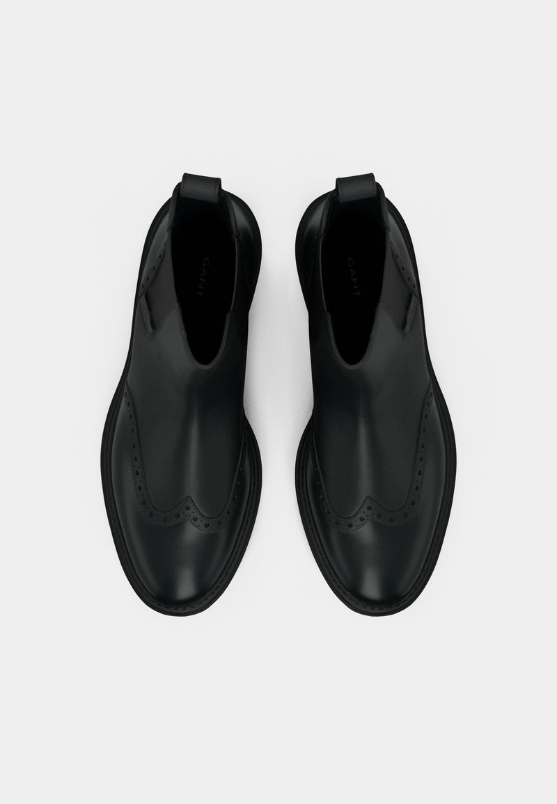 Schwarze Leder-Chelsea-Boots mit glatter Oberfläche, elastischen Seitenpaneelen, dekorativen Brogue-Details und einer leicht erhöhten Sohle.