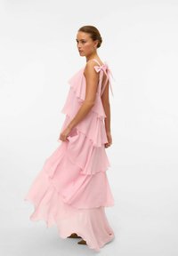 Abito maxi rosa con strati arruffati, spalline sottili e dettaglio a fiocco sul retro. Realizzato in tessuto leggero e trasparente.