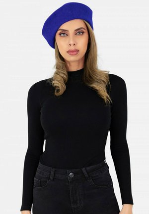 Haut à manches longues noir associé à un jean noir. Accessoirisé avec un béret en feutre bleu. Texture lisse avec un design ajusté et des détails subtils.