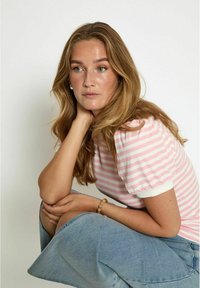 Gaiši rozā un baltās svītrās adīts tops ar īsām puff piedurknēm, savienots ar džinsim svārkiem. Aksesuāri ietver koka pērlīšu rokassprādzi.