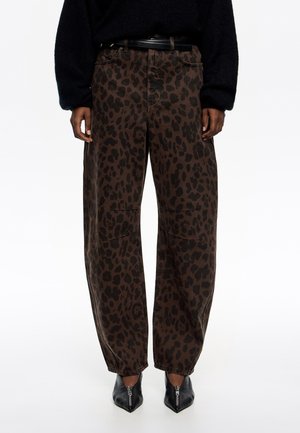 Pantalones de mezclilla de corte ancho con estampado de leopardo marrón, que presentan una cintura alta y cremallera. Zapatos negros de punta afilada completan el conjunto.