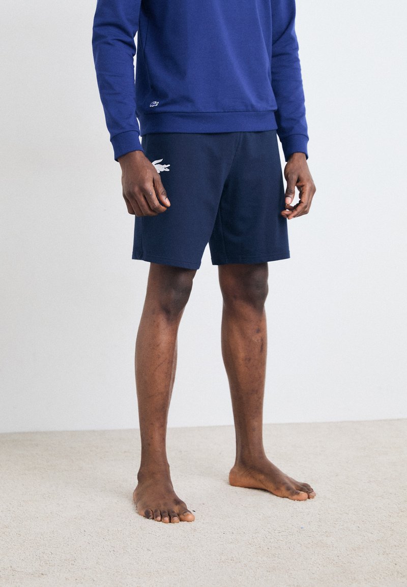 Dunkelblaues Sweatshirt kombiniert mit dunkelblauen Shorts mit einem weißen Logo. Der Stoff wirkt weich, strukturiert und eignet sich gut für legere Kleidung.