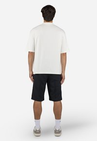 White short-sleeve shirt with relaxed fit, paired with black knee-length shorts. Footwear features a light gray and white color scheme.