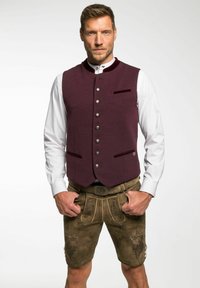 Bordeauxfarbener Wollwesten mit Stehkragen, silbernen Knöpfen und zwei Taschen. Kombiniert mit beigen Lederhosen mit gestickten Details.