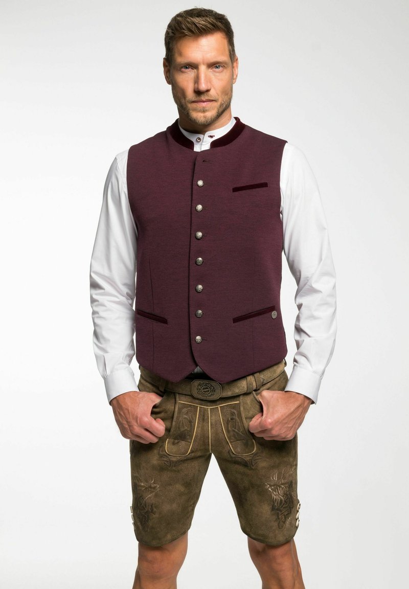 Bordeauxfarbener Wollwesten mit Stehkragen, silbernen Knöpfen und zwei Taschen. Kombiniert mit beigen Lederhosen mit gestickten Details.