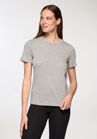 Szara koszulka z krótkim rękawem, wykonana z miękkiego materiału, z okrągłym dekoltem i luźnym krojem. W połączeniu z czarnymi legginsami.