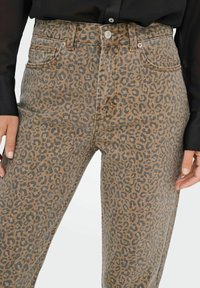 Džínové kalhoty s leopardím potiskem a vysokým pasem, s pevným zapínáním na knoflík, poutky na opasek a předními kapsami. Hnědo-černá barevná kombinace.