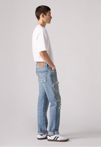 Witte oversized t-shirt met korte mouwen, lichtblauwe distressed jeans met scheuren en witte sneakers met zwarte strepen. Eenvoudig, casual ontwerp.