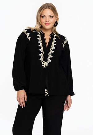Zwarte blouse met bloemenborduursel in wit en goud, met een placket-halslijn en lange mouwen, afgewerkt met een kwastaccent.