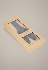 Szare szelki z srebrnymi klipsami, zapakowane w brązowe kartonowe pudełko z przezroczystym plastikowym okienkiem. Szelki mają skórzane elementy na paskach.