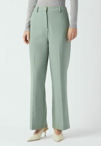 Svetlo zelene široke hlače iz gladkega tkanine z sprednjimi gubami in zankami za pas, kombinirane s kremnimi petkami.