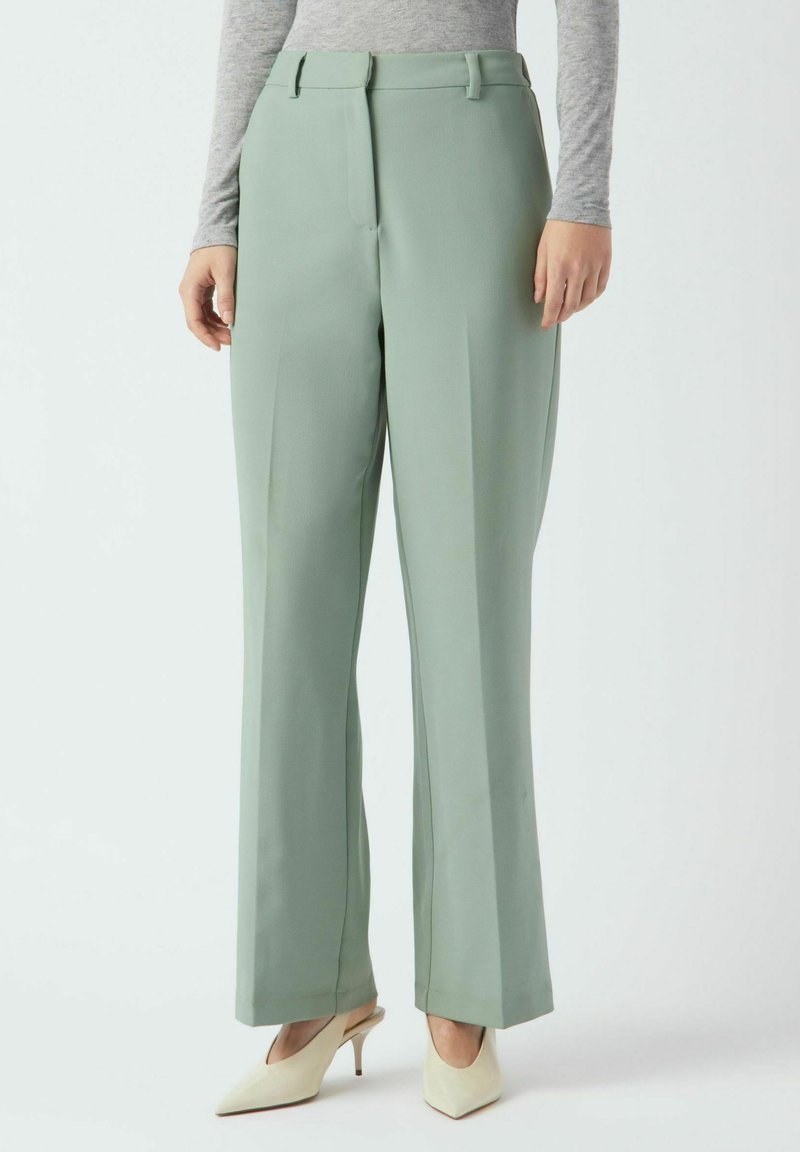Svetlo zelene široke hlače iz gladkega tkanine z sprednjimi gubami in zankami za pas, kombinirane s kremnimi petkami.
