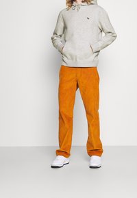 Grijze katoen hoodie met een verstelbare capuchon en kangoeroezak, gecombineerd met oranje corduroy broek en witte sneakers.