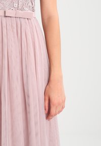 Lichtroze jurk met een kanten bovenstuk en een geplooide tule rok, afgewerkt met een bijpassende stoffen riem op de taille.