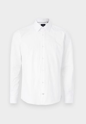 Balta garām piedurknēm krekls no kokvilnas. Iezīmēta ar pogām uz apkakles, priekšējo pogu aizdari ar rozā pogām un izliekta apakšmalu.