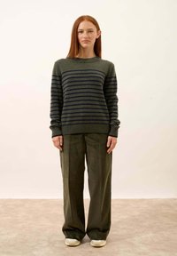 Khaki zielony sweter z dzianiny z granatowymi paskami, okrągły dekolt, ściągacze; noszony z spodniami w kolorze khaki o wysokim stanie i szerokimi nogawkami oraz sportowymi beżowymi trampkami.