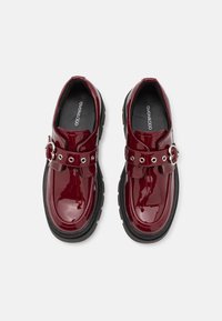 Burgundy lackläderskor med en kraftig svart sula, med en rem med spänne, rund tå och slät yta.