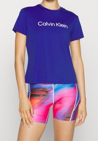 Camiseta azul de Calvin Klein con logo blanco, combinada con pantalones cortos de patrón abstracto y colorido en rosa y azul, con costuras blancas.