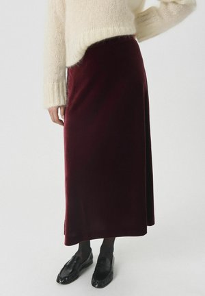 Kremfarvet strikket sweater kombineret med en lang bordeaux fløjlsnederdel, sorte strømpebukser og sorte loafers på en ensfarvet hvid baggrund.