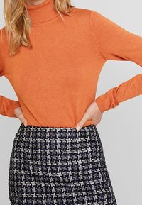 Pomarańczowy sweter z golfem, z prążkowanymi mankietami i dołem, w zestawie z teksturowaną dzianinową spódnicą w granatowo-białą kratkę.