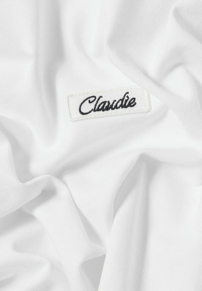 Tessuto bianco con una consistenza morbida e liscia, caratterizzato da un'etichetta ricamata "Claudie" nera su sfondo bianco.