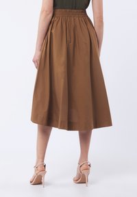 Jupe marron de longueur mi-mollet avec taille froncée, en tissu léger ; elle dispose de deux poches sur les côtés et a une texture lisse.