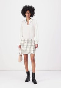 White blouse with pleated sleeves, paired with a textured tweed skirt in cream and pastel colors. Black ankle boots and a small pink bag.