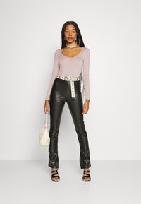 Blusa de manga longa cor malva com decote arredondado, combinada com calças pretas de couro sintético de cintura alta, apresentando um cinto branco e detalhes em botão.