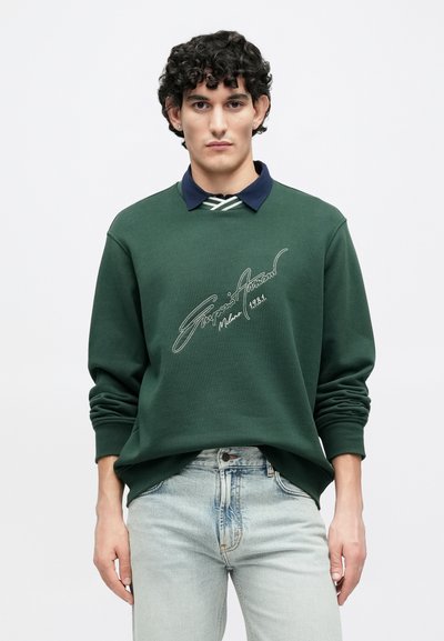 Πράσινο φούτερ με ναυτικού χρώματος γιακά, με λευκό κεντημένο λογότυπο στο μπροστινό μέρος. Το ύφασμα φαίνεται απαλό, με ριμπ μανσέτες και τελείωμα.