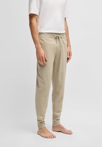 Beige sweatpants met een trekkoord in de tailleband, tapered leg ontwerp en een zachte textuur. Gecombineerd met een effen wit t-shirt met korte mouwen.