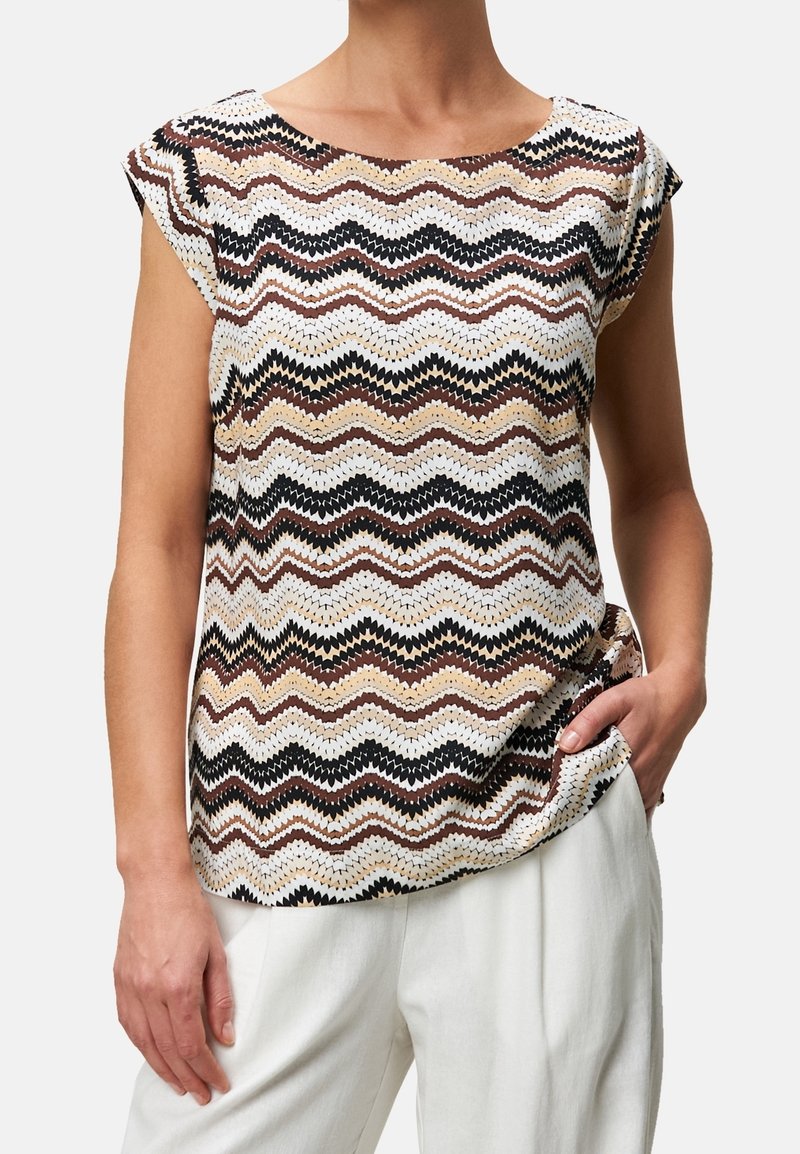 Haut à manches courtes en tissu texturé présentant un motif en zigzag dans des tons blanc, beige, marron et noir. Coupe décontractée avec poche latérale.