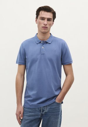 Polo shirt albastru deschis cu guler, închidere cu trei nasturi și logo brodat. Asortat cu blugi din denim, cu o croială lejeră.