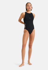 Maillot de bain noir une pièce avec un col haut, fermeture éclair sur le devant, et une coupe cintrée. Présente un logo latéral de couleur contrastante. Texture lisse.