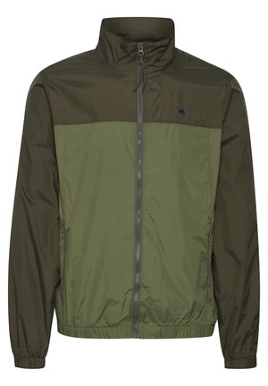 Chaqueta ligera de color verde oliva con cremallera frontal, cuello alto, puños elásticos y un diseño en dos tonos con paneles de verde más oscuro y más claro.