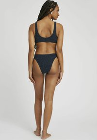 Ensemble bikini bleu marine composé d'un matériau texturé et pailleté. Le haut a des bretelles larges, et le bas présente un design échancré avec un creux à l'arrière.