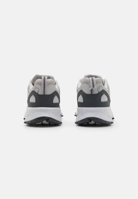 Zapatillas deportivas en gris y blanco con parte superior de malla, suela acolchada, suela prominente y detalles reflectantes en la parte trasera.